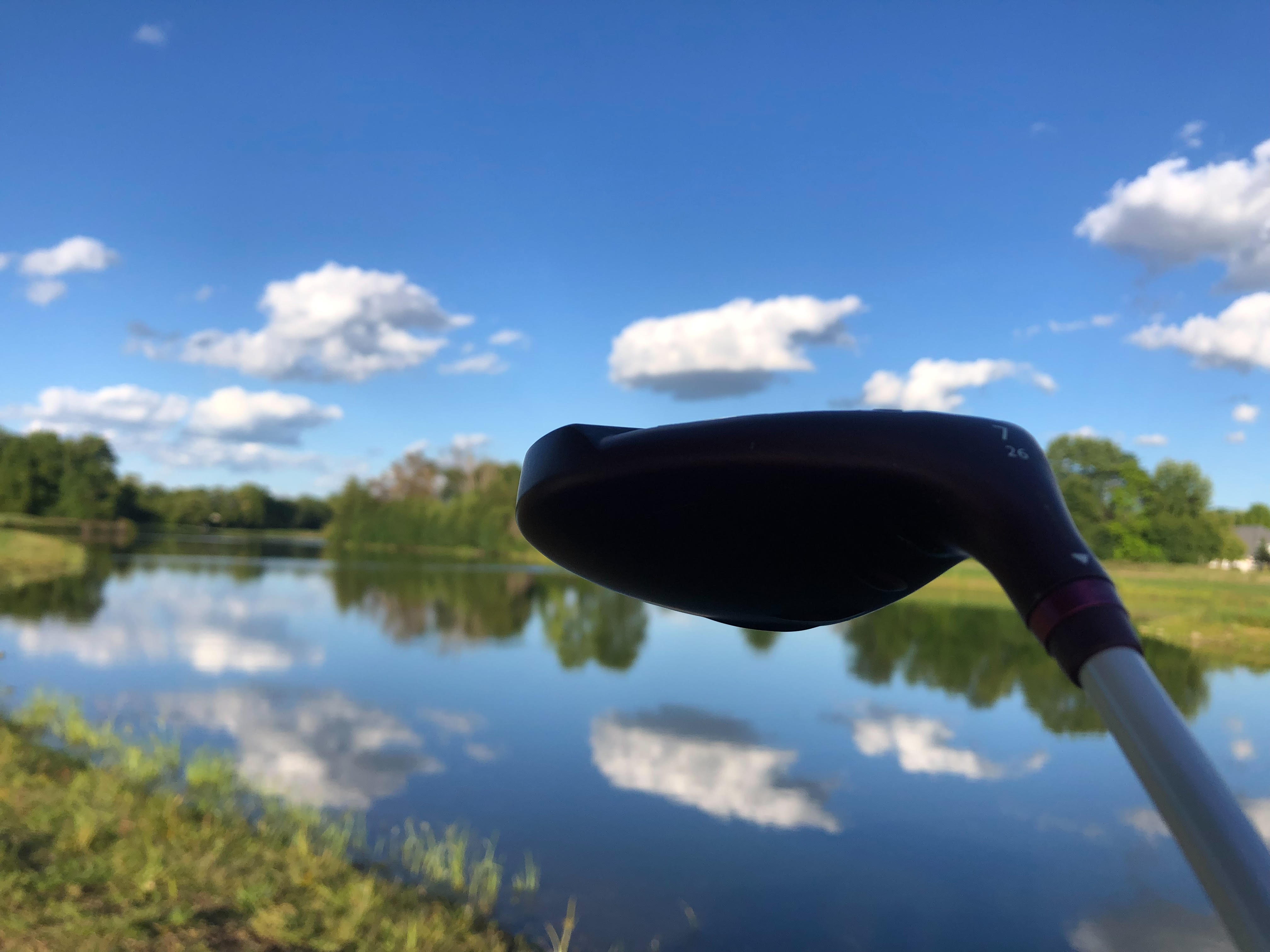 Golf club close to camera in image overlooking pond on golf course