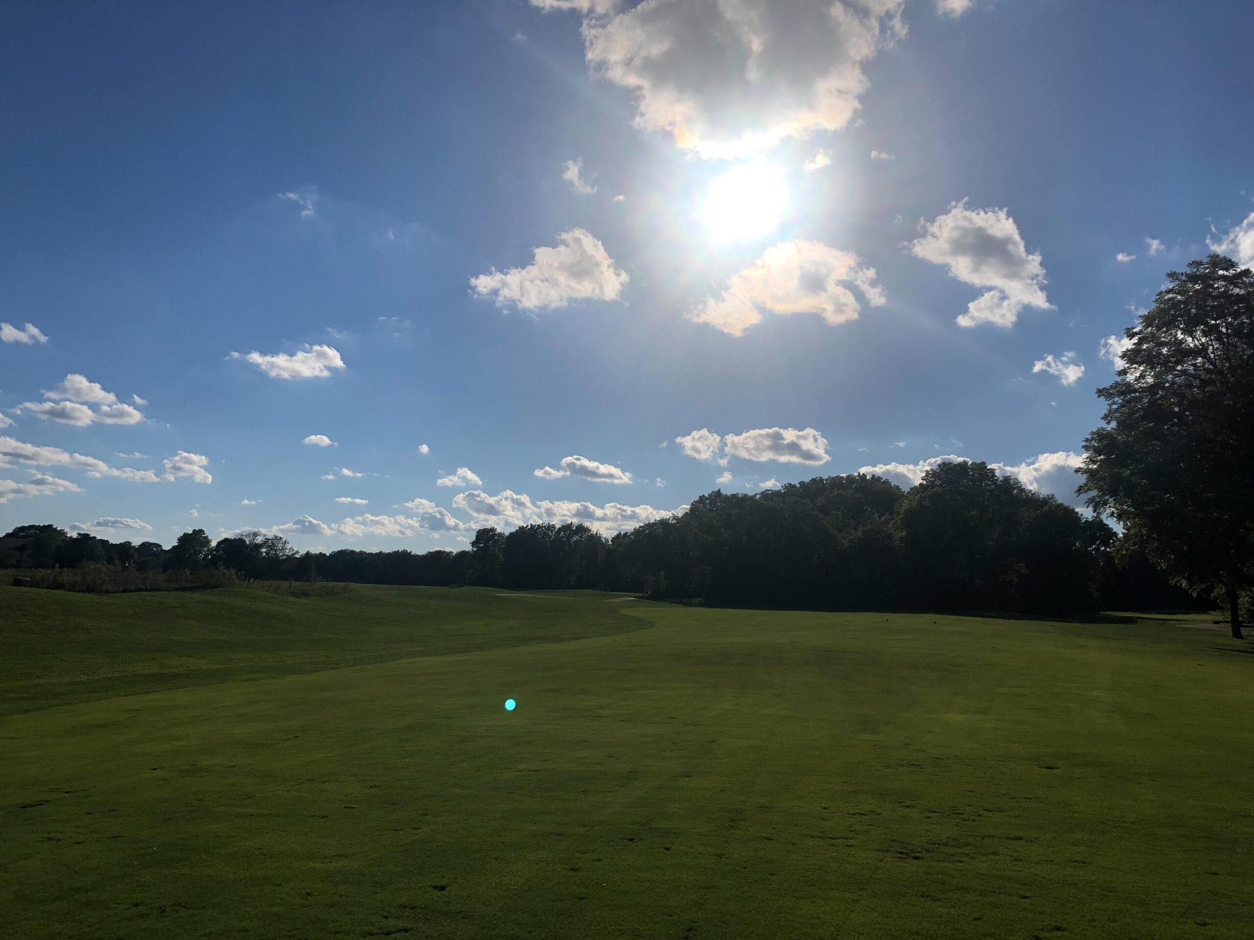 View of golf course with trees and sun shining in the sky